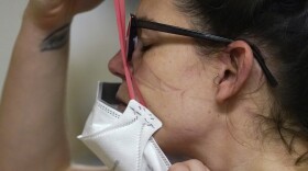 FILE - Registered nurse Jessalynn Dest pulls on a new N95 mask as indentations remain from another she had just removed after leaving a COVID-19 patient room in the acute care unit of Harborview Medical Center, Jan. 14, 2022, in Seattle. The Biden administration will begin making 400 million N95 masks available for free to Americans starting next week, now that federal officials are emphasizing their better protection against the omicron variant of COVID-19 over cloth face coverings.  The White House announced Wednesday that the masks will come from the government's Strategic National Stockpile, which has more than 750 million of the highly protective masks on hand.  (AP Photo/Elaine Thompson, File)