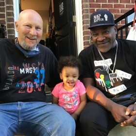 Mike sits on the front stoop with Theo Hill and Theo's granddaughter, Miracle