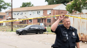 A police officer goes under tape that marks off Glade Court in Brooklyn after a shooting early Sunday morning. (Jessica Gallagher/The Baltimore Banner)