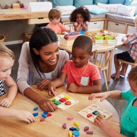 Teacher And Pupils Using Wooden Shapes In Montessori School