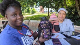 Admire Stewart and Margie Rodriguez hold up water bottles that Rodriguez purchased for housekeepers at the University of Maryland. Hydration is a challenge when the housekeepers work long hours in unairconditioned dormitories across campus.