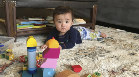 An infant on a rug with blocks in front of him and books and furniture behind him.