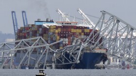 A boat moves past a container ship as it rests against wreckage of the Francis Scott Key Bridge on Tuesday, March 26, 2024, as seen from Pasadena, Md. The container ship lost power and rammed into the major bridge in Baltimore early Tuesday, causing it to snap and plunge into the river below. Several vehicles fell into the chilly waters, and rescuers searched for survivors. (AP Photo/Mark Schiefelbein)