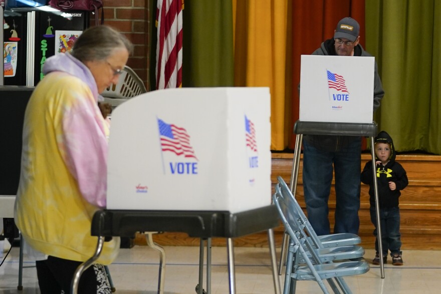 Jacob Lewis, 3, bottom right, waits at a privacy booth as his grandfather, Robert Schroyer, top right, fills out his ballot while voting at Sabillasville Elementary School, Tuesday, Nov. 8, 2022, in Sabillasville, Maryland.