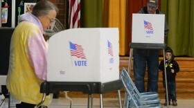 Jacob Lewis, 3, bottom right, waits at a privacy booth as his grandfather, Robert Schroyer, top right, fills out his ballot while voting at Sabillasville Elementary School, Tuesday, Nov. 8, 2022, in Sabillasville, Maryland.