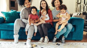 Multi-ethnic mommies sitting with children. Young mothers with babies sitting on sofa and looking at camera.