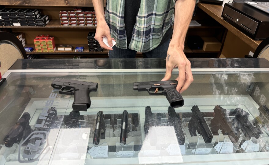 Theodore Daniels displays two of Worth-A-Shot's bestselling handguns, the Glock 43X and the Sig Sauer P-365 Rose, a special edition marketed to women. Photo by Rachel Baye/WYPR.