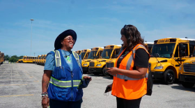 Donna McSee and Jackie Scott, drivers for Howard County Public Schools employed by Zūm, talk in front of a line of brand new yellow school buses at Zūm’s Jessup operations hub on Aug. 22. (Daniel Zawodny/The Baltimore Banner)